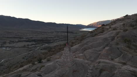 panoramic view of a cross on a rocky hill at dusk overlooking a valley and lake