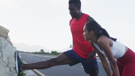 diverse couple exercising stretching during run on a mountainside country road