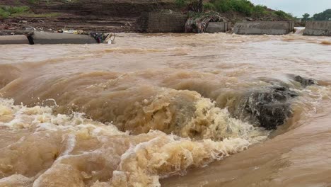 static shof of intense flooding in a river and turbulent, muddy water flowing rapidly in higher volume and swift current, submerged concrete structures indicating a bridge or dam overwhelmed by flood