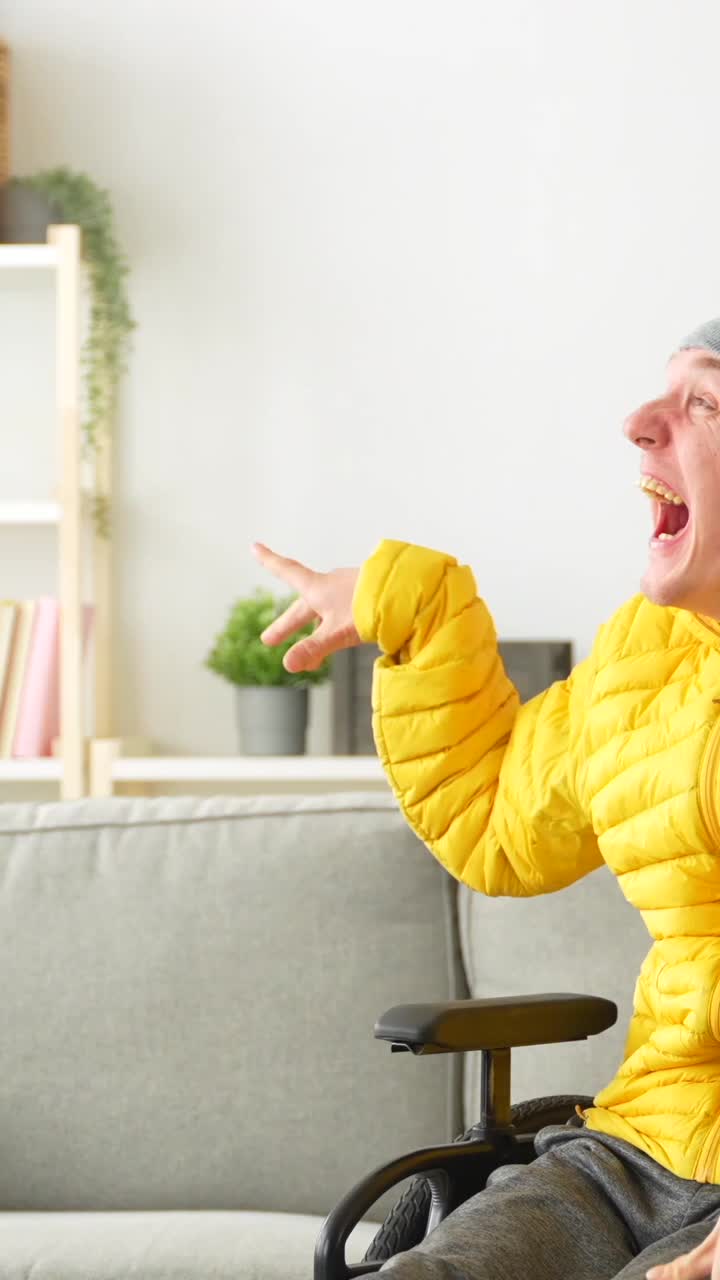 Man in yellow jacket and beanie sitting on couch and wheelchair