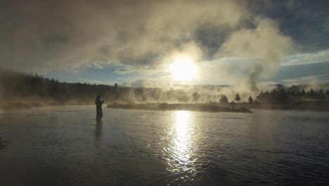 side angle silhouette of a man with fishing rod in his hand standing in river illuminated by shiny sunlight and smoke, pov