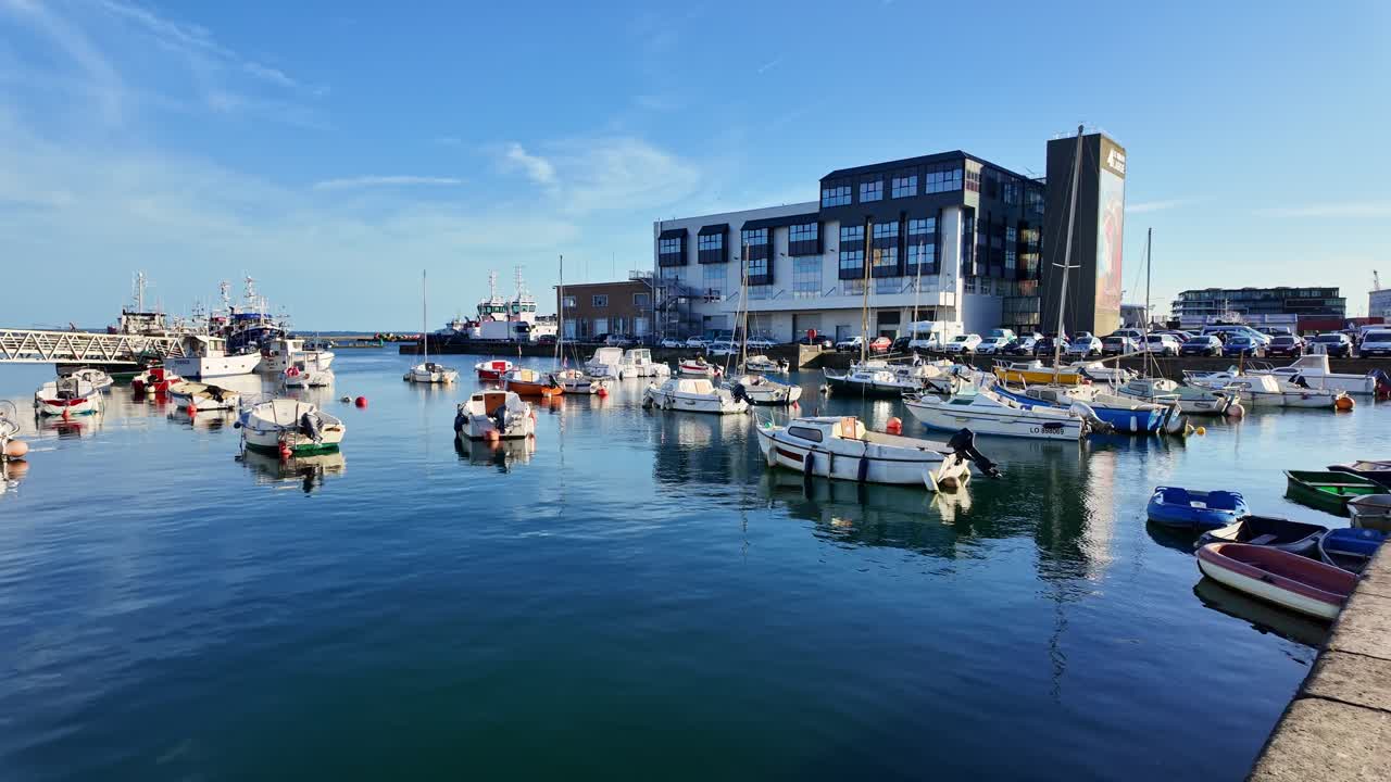 Panning view of Brest harbor with moored boats, the maritime building in the background, and clear blue water under a sunny sky - Brittany France