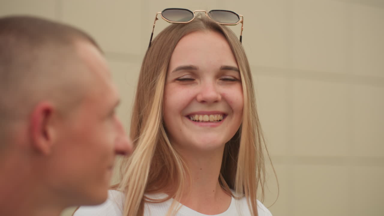 Donna su un tetto che ride con il partner, vista sulla città, occhiali da sole sulla testa, luce solare sui capelli, scatti spontanei di profilo, brezza leggera, ringhiera del terrazzo, sfondo architettonico, connessione calorosa, atmosfera estiva rilassata
