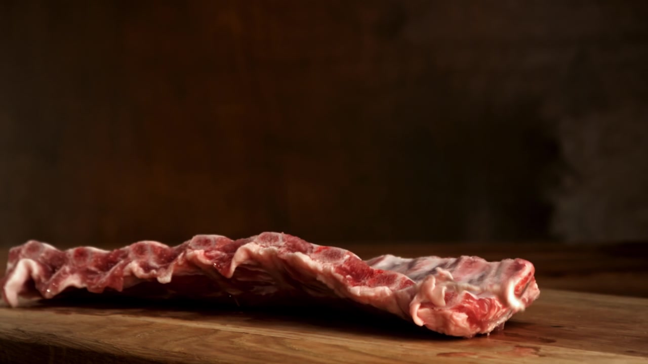 Costine di maiale fresche e crude che cadono su un tagliere di legno al rallentatore.