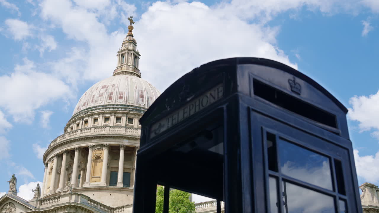 Black telephone booth with the dome of St. Paul's Cathedral towering behind against a bright sky in London, England