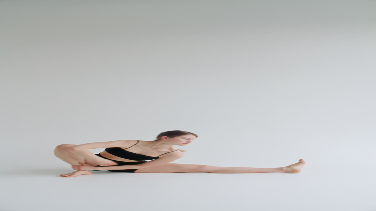 Mädchen dehnt sich in fortgeschrittenen Yoga-Posen in einem Studio mit weißem Hintergrund