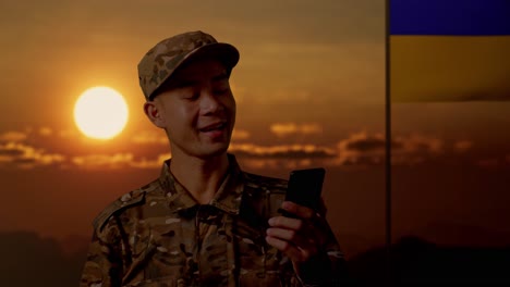 soldier communicating via smartphone during sunset with ukrainian flag in background