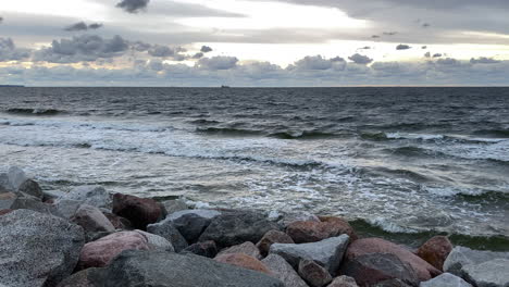 cloudscape over the splashing waves of the ocean at the rocky coastline through dusk