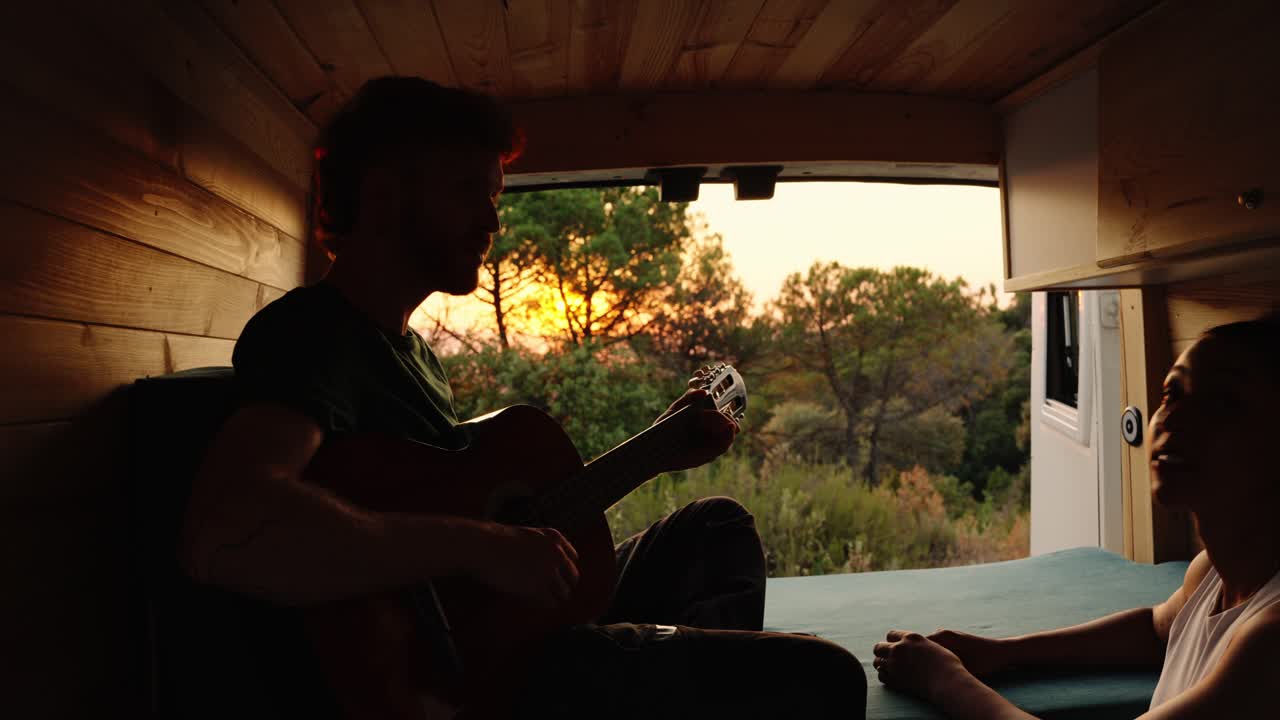 Man playing guitar in a van at sunset