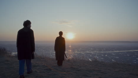 couple walking to frozen lake, holding hands and watching sunset