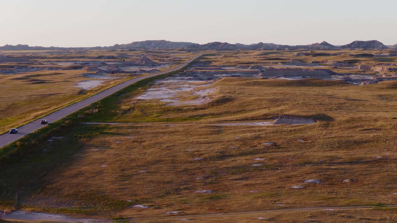 Road Leading Into Golden Horizon Over Rugged Badlands From Drone View
