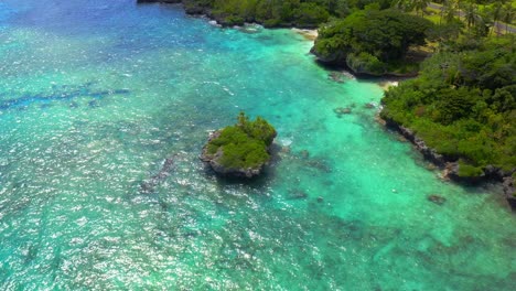 the camera gracefully glides towards a small, rocky island surrounded by a serene blue lagoon, gently lapping against the idyllic white-sand beach