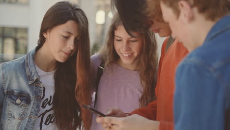 un grupo de adolescentes con dos chicas y dos chicos viendo algo en la pantalla de un teléfono móvil 1