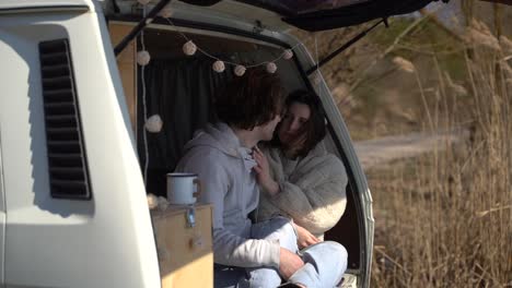 una joven pareja enamorada en la parte trasera de una caravana junto a un lago.