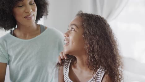 Happy-african-american-mother-and-daughter-brushing-hair-in-bedroom,-slow-motion