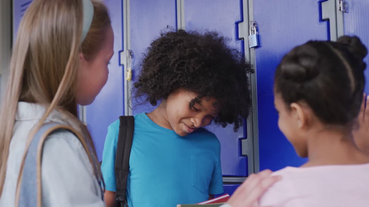 Video of three happy, diverse schoolgirls talking by lockers in school corridor, copy space