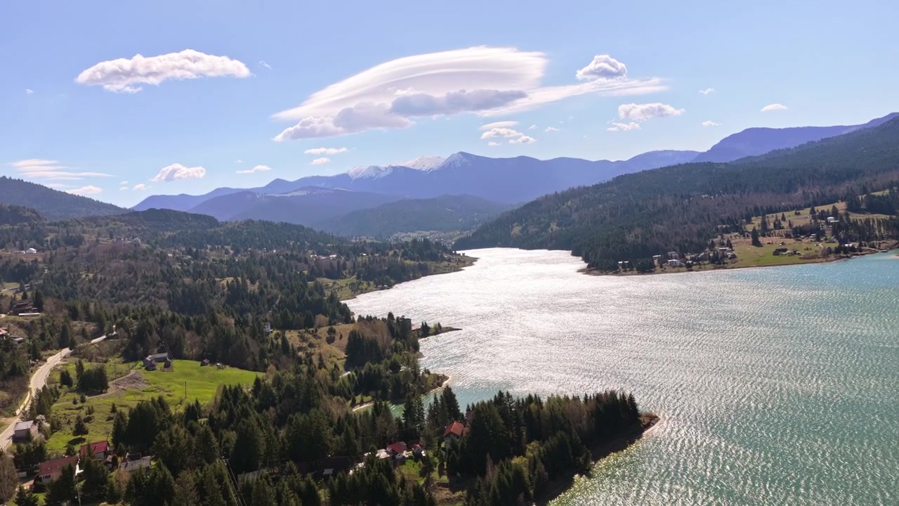 Veduta aerea con drone del lago Colibita con acque turchesi, circondato da colline boscose e case di montagna sparse