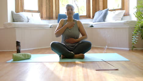 Varitas-De-Incienso-Con-Estelas-De-Humo-Sobre-Una-Mujer-Birracial-Senior-Enfocada-Meditando-En-Casa