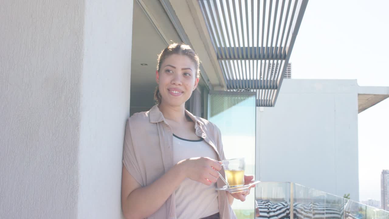 Video verticale: Donna appoggiata che mescola una tazza con un cucchiaino sul balcone, la luce del sole attira il suo sguardo