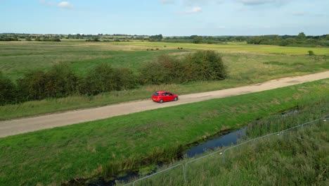 Coche-Rojo-Conduciendo-Por-La-Campiña-Inglesa-En-Norfolk,-Reino-Unido