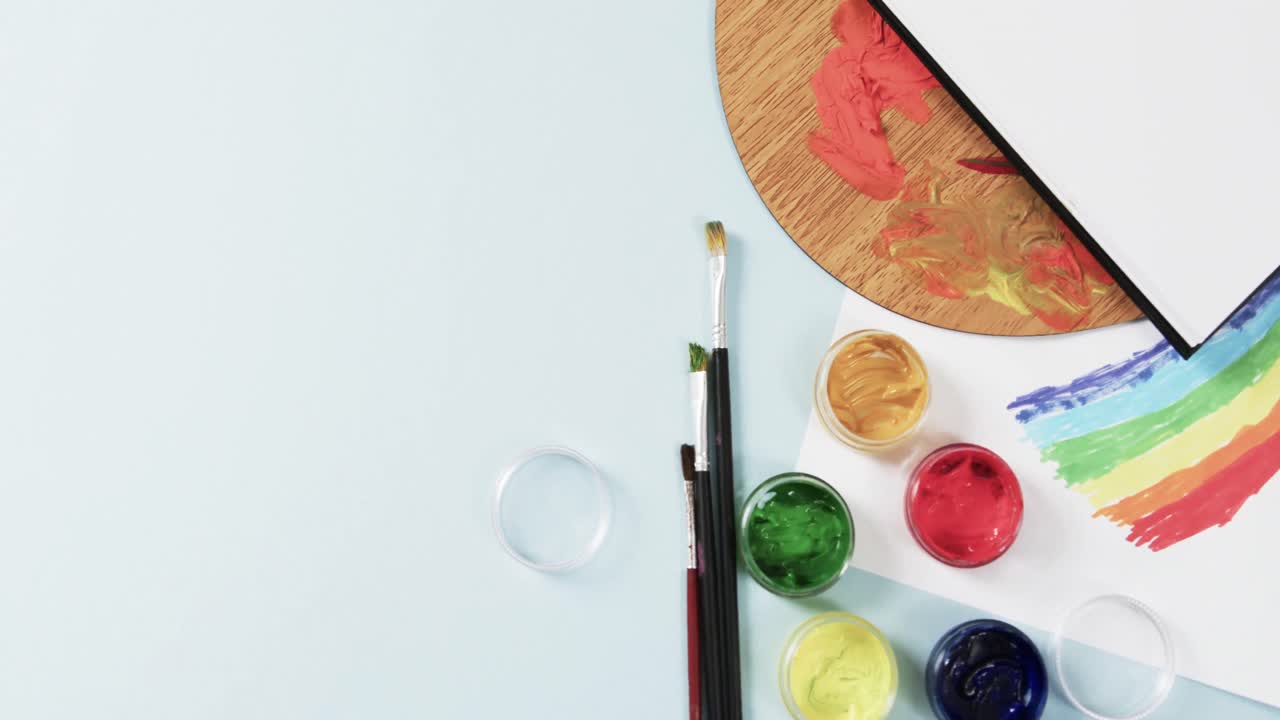 슬로우 모션으로 파란색 배경에 노트북, 브러시 및 페인트의 오버헤드 뷰