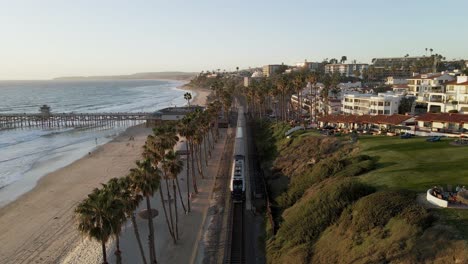 flying over railroad at sunset, san clemente pier beach, california, aerial wide slow motion shot