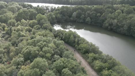 Radfahrer,-Der-Einen-Langen-Naturpfad-Radelt,-Der-Von-Einem-See-Und-Bäumen-Umgeben-Ist