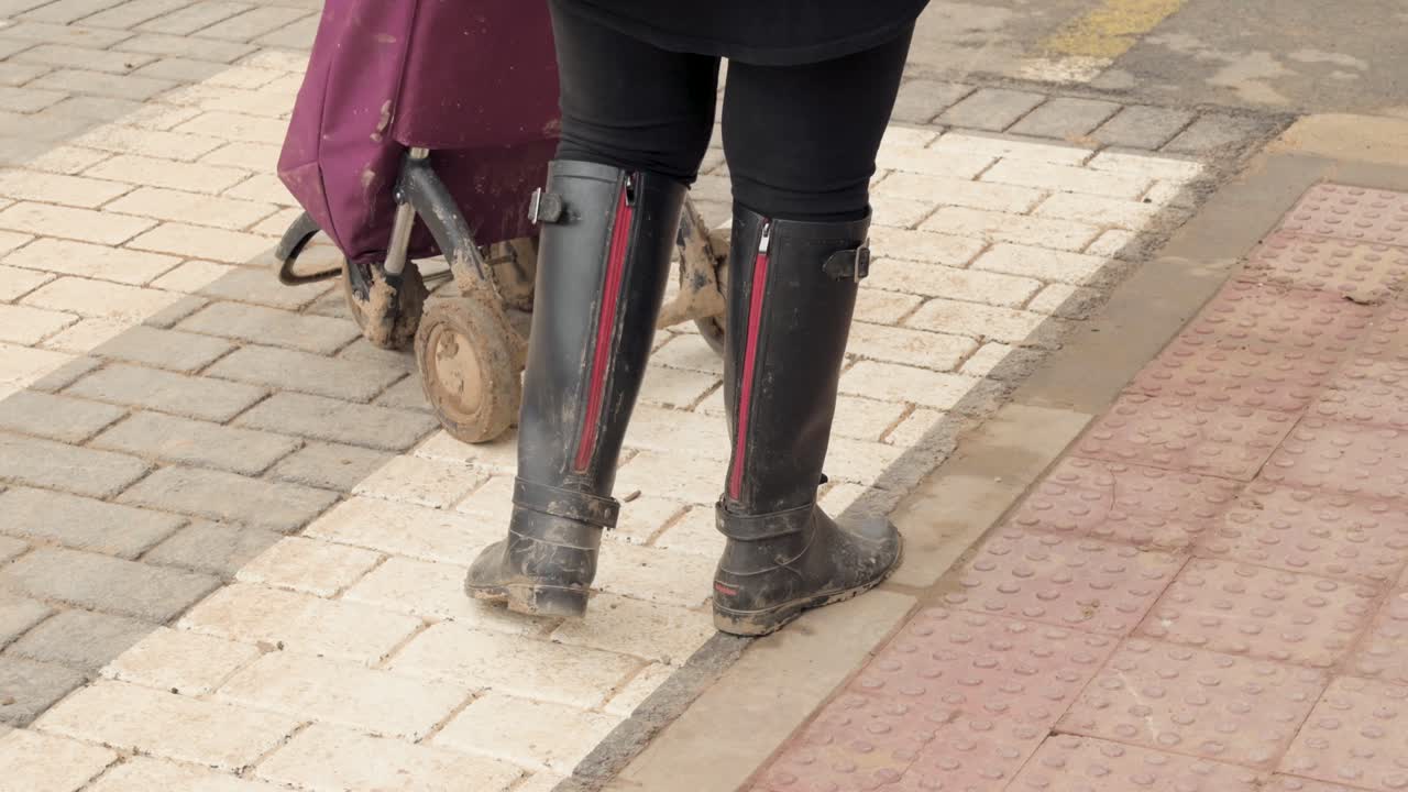 Woman in Muddy Rain Boots Walking with Shopping Cart
