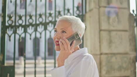 mature lady having conversation on sunny street closeup. relaxed pensioner call