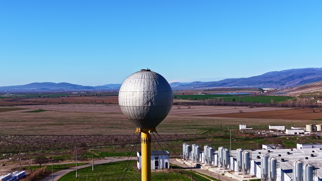 Vista de uma grande estrutura esférica em um poste alto com campos e colinas no plano de fundo durante um dia claro