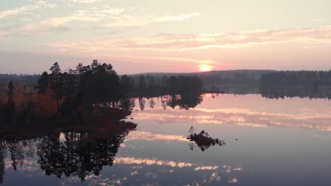 Vista-Aérea-Panoramización-Lateral-Cinemática-De-Un-Lago-Perfectamente-Reflejado-En-Un-Bosque-Durante-La-Puesta-De-Sol-Y-El-Otoño