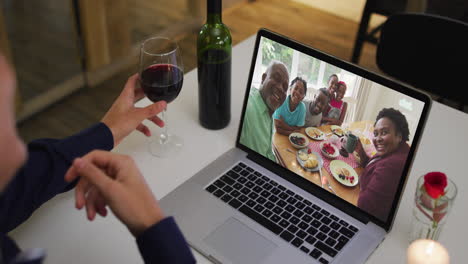 sección media de una mujer afroamericana bebiendo vino mientras hace una videollamada en una computadora portátil en casa