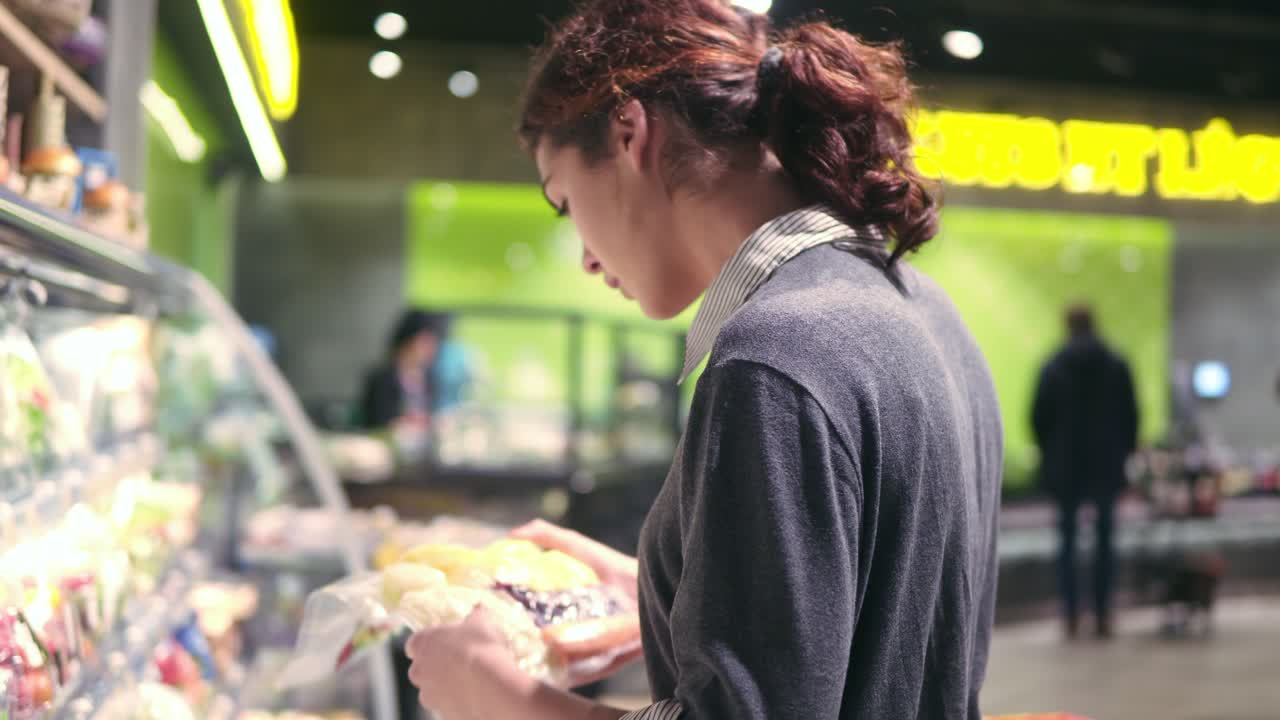 Young beautiful brunette girl in her 20's takes prepacked vegetables from the shelf at the fruit and vegetable aisle in a supermarket.