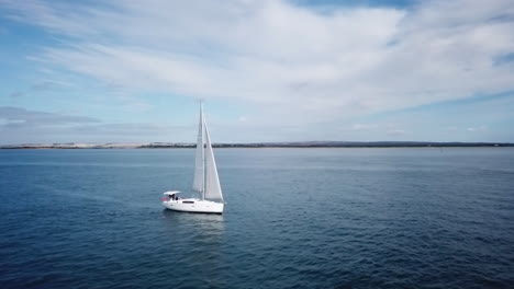 aerial footage panning around luxury yacht sailing slowly in deep blue water near shore