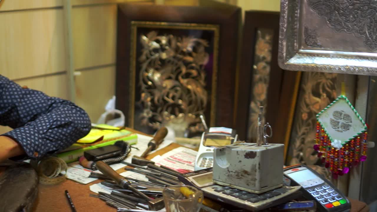 Static shot slowly panning out, showing an artist working on Qalam Zani, Isfahan famous handicrafts. Isfahan artists perform engraving, grating on a variety of objects including decorative items.