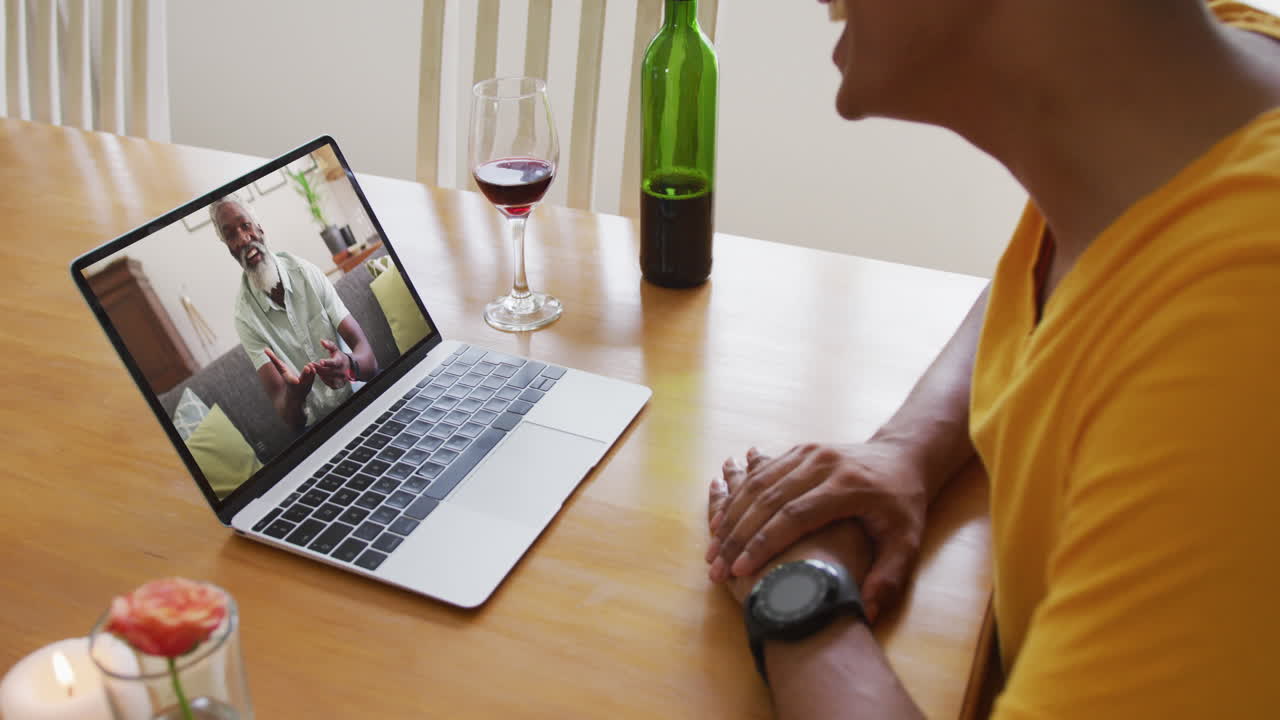 Mixed race man sitting at table using laptop making video call with male friend
