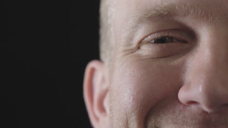 close up portrait of young man eye looking at camera smiling happy caucasian male half face  isolated on black background