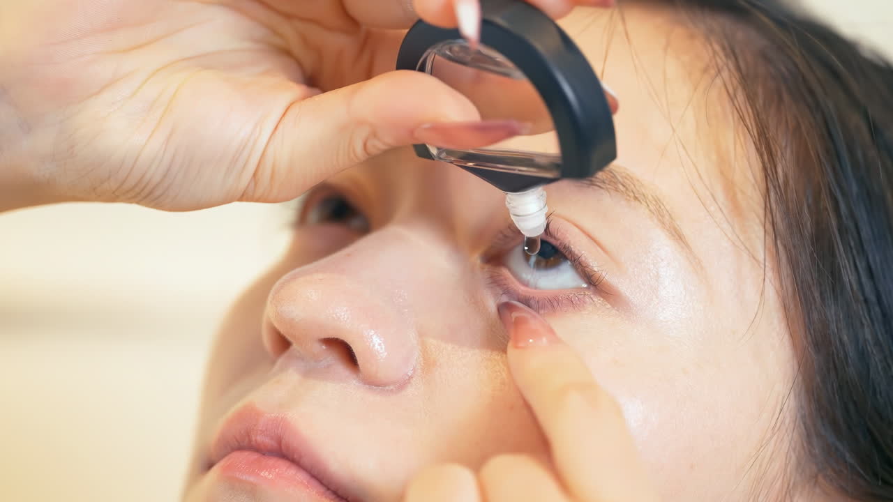Eine junge Frau tropft sich nach einem langen Arbeitstag am Computer im Büro Augentropfen in ihre trockenen, gereizten Augen. Eine Dame verwendet Augentropfen mit Antihistaminika und ophthalmischen Antibiotika zur Behandlung von Infektionen.