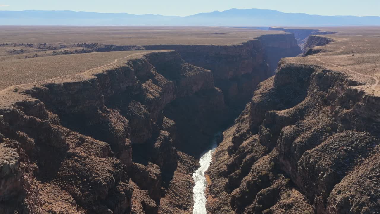 High-angle aerial view capturing the deep, winding channel of the Rio Grande River cutting through the massive geological canyon walls. Highlights the arid beauty of the American Southwest