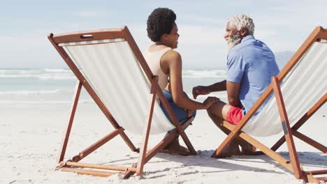 African-american-couple-holding-hands-and-lying-on-sunbeds-on-sunny-beach