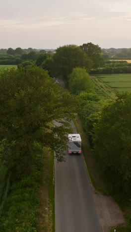 vertical drone shot of a rv driving through a alley on the countryside, sunset