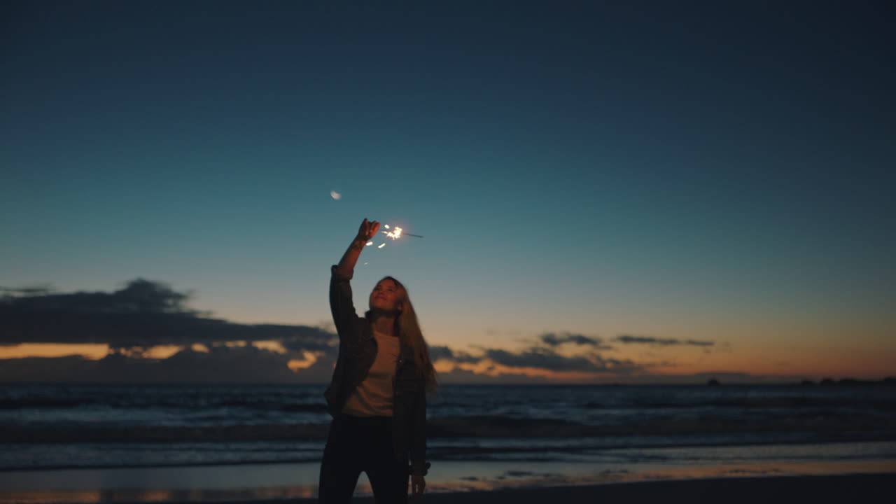 mujer jugando con bengala en la playa al atardecer celebrando la víspera de año nuevo niña divirtiéndose bailando agitando fuegos artificiales bengala disfrutando de la celebración junto al mar