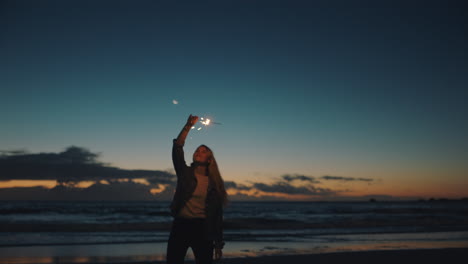 woman playing with sparkler on beach at sunset celebrating new years eve girl having fun dance waving sparkler firework enjoying celebration by the sea