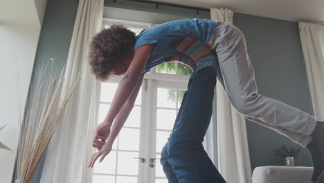 father lying on his back on the floor in the living room lifting his pre-teen son in the air with his legs, side view, low angle