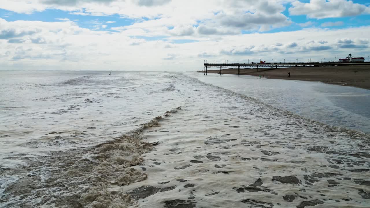 Typical English seaside resort, aerial shot using a drone, giving a high aerial viewpoint showing a wide expanse of sandy beach with a pier and crashing waves