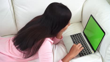 joven asiática usando un dispositivo portátil con pantalla verde. mujer asiática trabajando portátil mientras está sentada en el sofá en la sala de estar en casa. llave de croma.