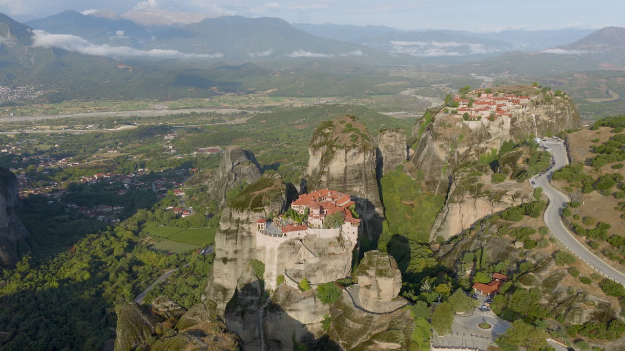 Cinematic aerial view of Meteora monastery in Greece perched on towering cliffs, dramatic rock formations and lush green valley create a breathtaking historic scene