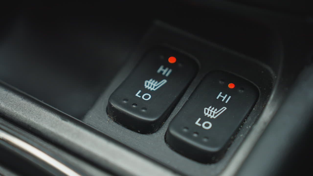 Close up of person activating seat heating button with red indicator light on car interior center console showing finger press detail of heating level control interaction and cabin feature