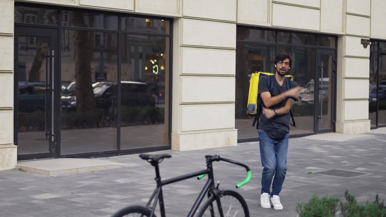 A bearded guy with a backpack is fooling around and dancing, slow motion