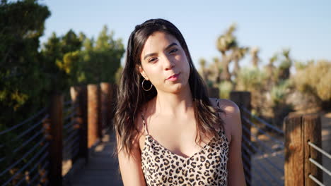 attractive hispanic woman walking in slow motion along a wooden path outdoors in sunlight smiling and happy